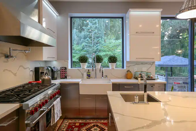 Cocina a medida con frentes blancos, encimera de piedra y ventana sobre el fregadero