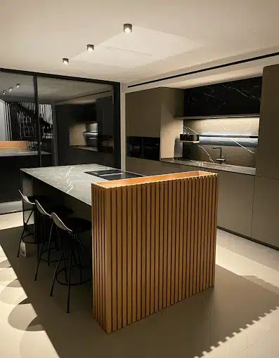 Cocina con isla de mármol y frontal de lamas de madera, frentes grises mate y encimera negra